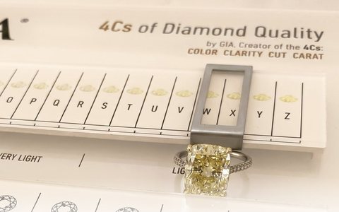 Warm-toned rectangular diamond ring resting on a GIA color comparison chart.